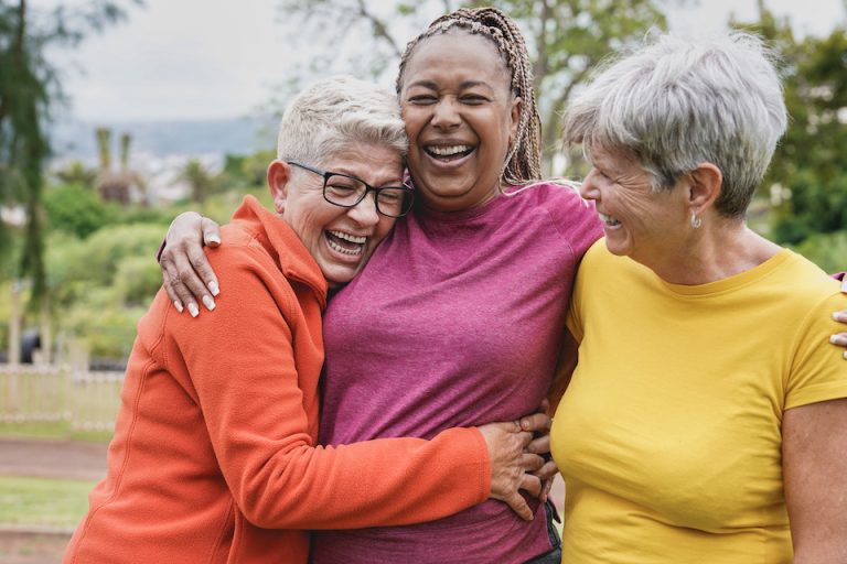 Happy multiracial senior women having fun together at park - Elderly generation people hugging each other outdoor